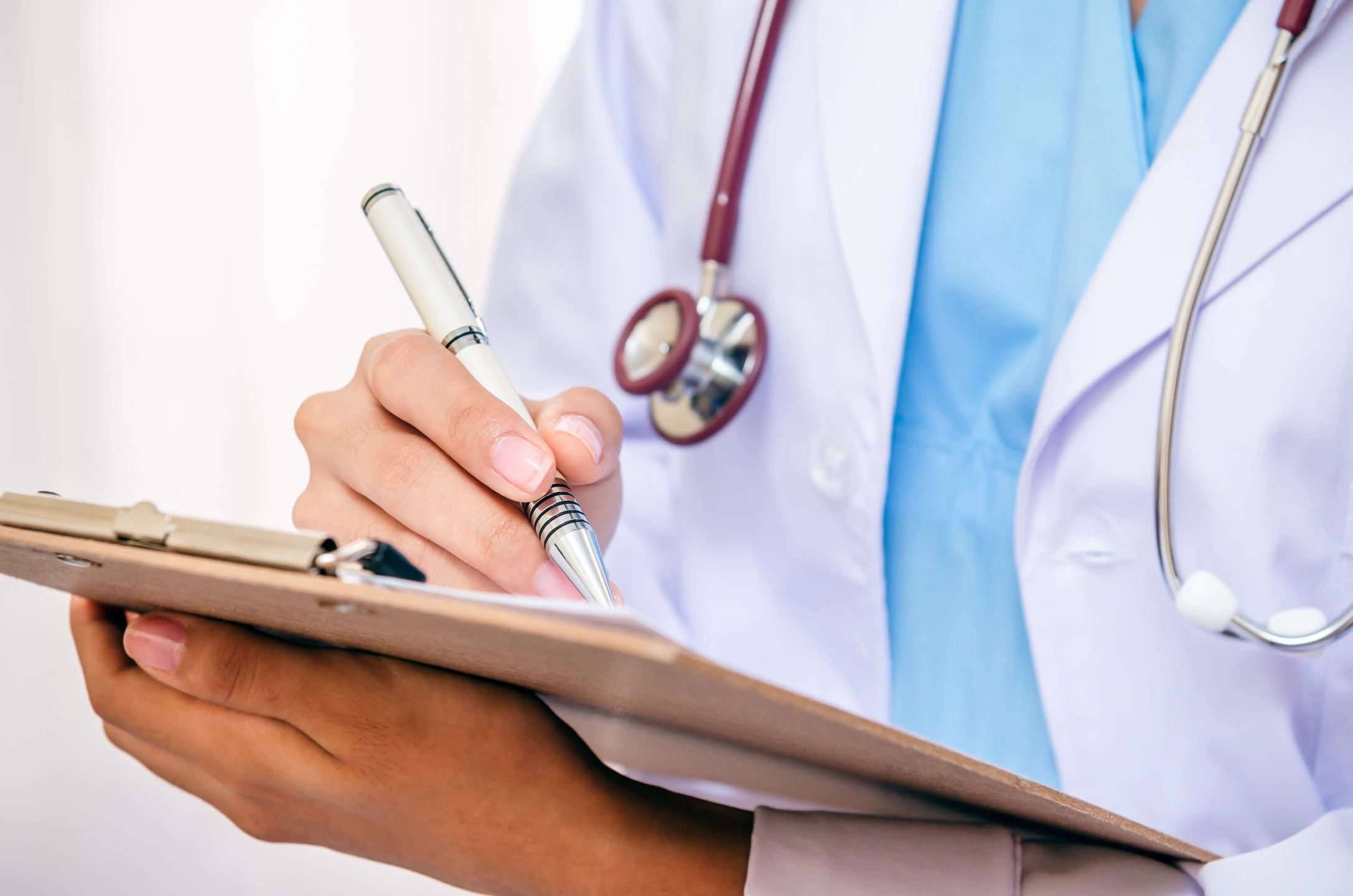 Person wearing white lab coat and stethoscope writing on clipboard